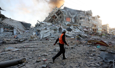 A man in an orange vest walks past the rubble of a building