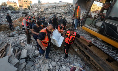 Men in emergency worker vests carry shrouded body away from destroyed building