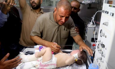 An emotionally distraught man caresses a baby lying in a hospital bed