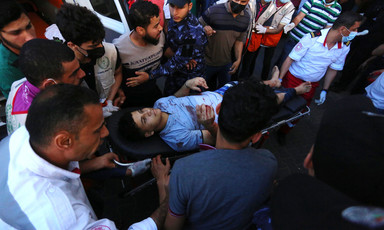 A young man with bloodied clothes lies on a stretcher amid crowd next to ambulance