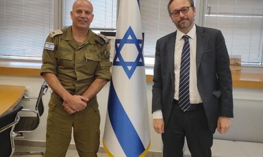 Man wearing military uniform stands beside man wearing suit 