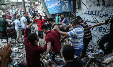 Men carry body of Yousif Abu Hussein as crowd on debris-strewn street looks on