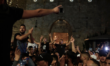 Men carried on shoulders in crowd make victory signs with their hands in front of Old City wall