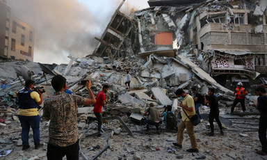 People stand by a pile of grey rubble from destroyed building 