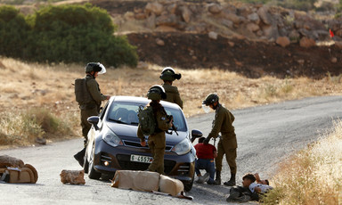 Four soldiers detain youths lying on the street next to a car