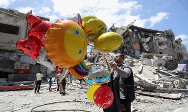 A man holds large, colorful balloons against a backdrop of ruins 