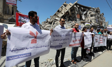 A group of people stand with placards beside a destroyed building 