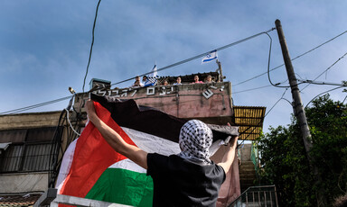 A man holds a flag up as people on top of a building look down