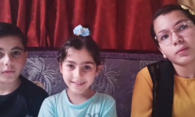 A boy and two girls are seated next to each other on a couch 