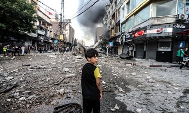 A boy stands in debris-strewn street with smoke on the horizon