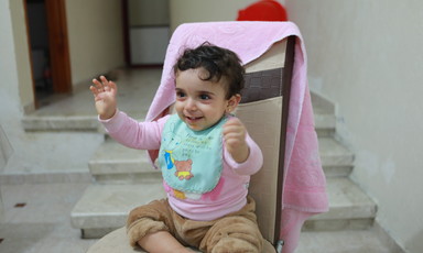 A young child sits on a chair and smiles 