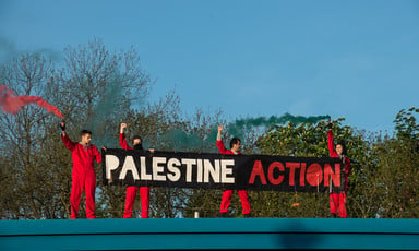 Four red-suited people hold a banner reading "Palestine Action"