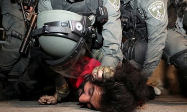 Police in riot gear hold the head of a pinned-down man to the ground