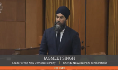 A man in a suit speaks at a microphone