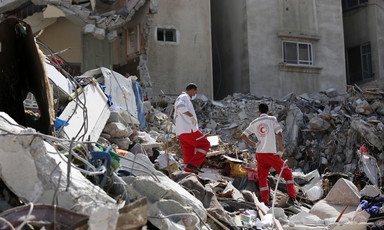 Two health workers stand in the rubble of a destroyed building 