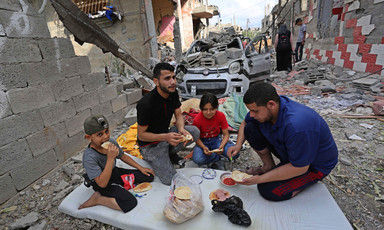 Two adults and two children eat a meal amid buildings that have been destroyed