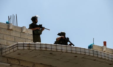Two armed officers stand on the roof of a brick building 