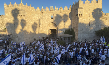 Large group of people with flags against backdrop of ancient stone wall