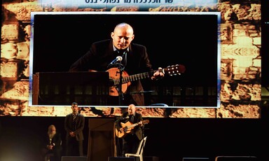 A giant screen shows man playing guitar as three people stand on stage beneath