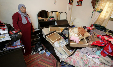 Woman stands next to bed piled up with dresser drawers, blankets and clothing