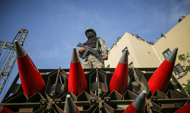 Man stands on truck carrying missiles as people watch from building