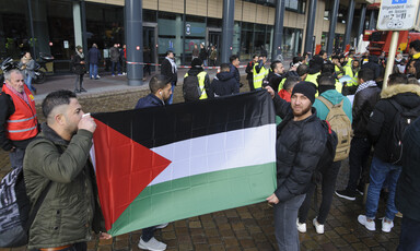 Two men hold flag, surrounded by a group of other people 