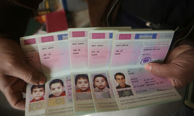 A pair of hands holds five passports opened to page showing photos