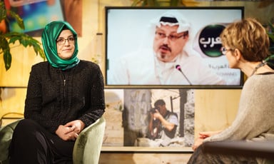 Two women in chairs converse front of screen that shows Jamal Khashoggi