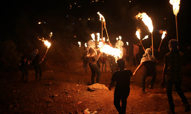 A group of men with lit torches walk across a field in the night