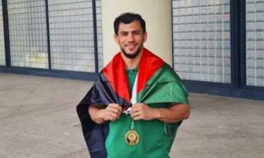 The Palestinian flag is draped around the shoulders of a smiling man 