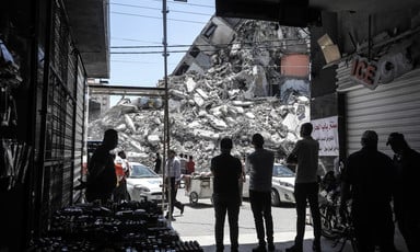 Silhouetted people stand in front of giant mound of rubble from a destroyed building