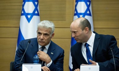 Two seated men with Israeli flags behind them confer
