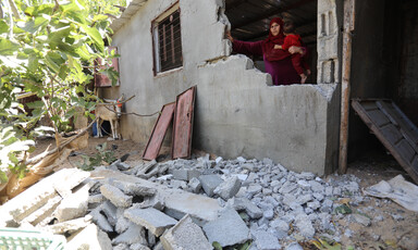 A woman stands behind the remains of a wall of her home