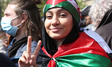 A woman draped in the Palestinian flags gives the victory sign