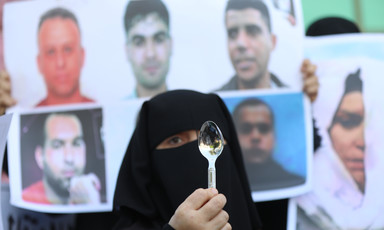 A woman standing by pictures of escaped men holds a spoon