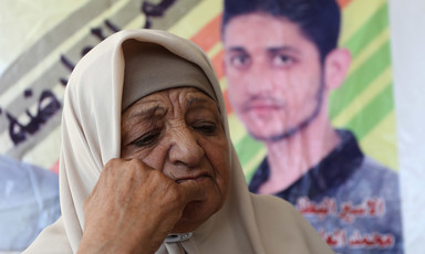 A woman rests her face on her fist with a poster of a man behind her 