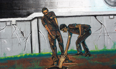 Mural depicts two men reaching out for a hand in a hole in the ground 
