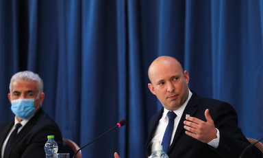 Naftali Bennet gestures with hand while sitting at table as Yair Lapid looks on.