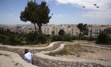 Helicopters fly over buildings, as a man looks on 