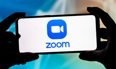 Fingers hold a smartphone displaying Zoom logo