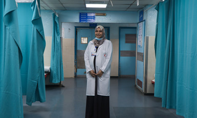 Woman wearing white coat stands in a hospital ward 