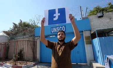 A man holds the Facebook logo upside down in front of the UNSCO building
