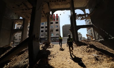 Two men stand on sand inside concrete skeleton of badly damaged building