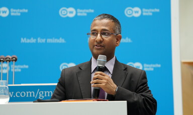 Man in suit stands at podium holding microphone