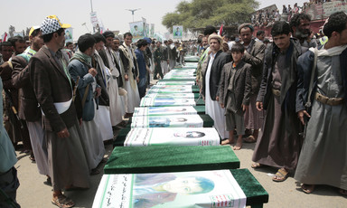 Men stand on either side of a row of coffins draped with banners showing portraits of the slain children