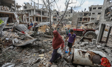 Woman and boy walk through street filled with rubble and lined by bombed-out apartment blocs