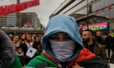 Close up of man in face mask and hoodie carrying Palestinian flag