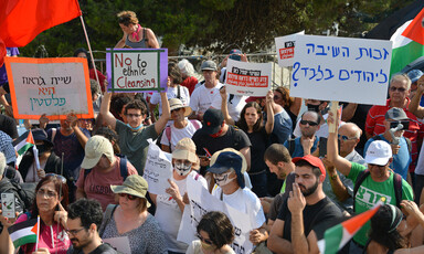 A crowd of protestors hold up the Palestinian flag and signs in Hebrew and English