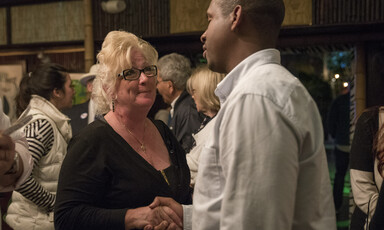 A man and a woman shake hands with people in background