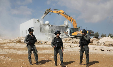 Three armed men stand in front of half destroyed house and construction machine